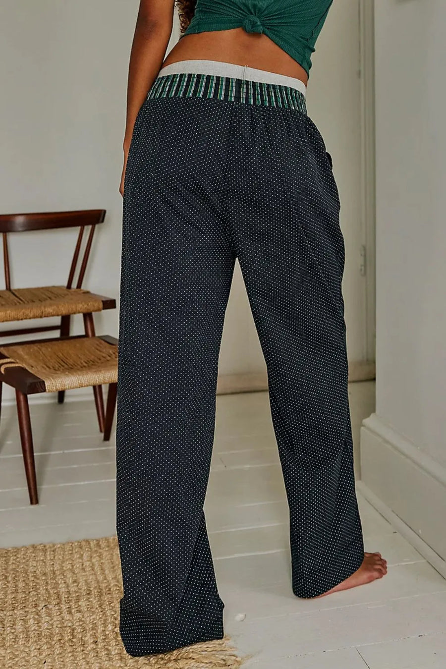 Person wearing black patterned pants and a green top in a room with wooden furniture.