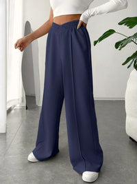 Person wearing navy wide-leg pants and a white top in a minimal indoor setting.
