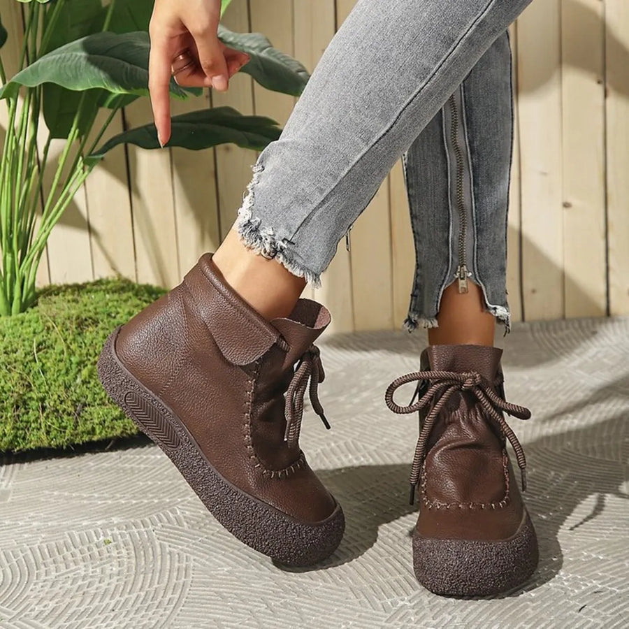 Brown leather boots worn with light blue jeans on a textured surface.
