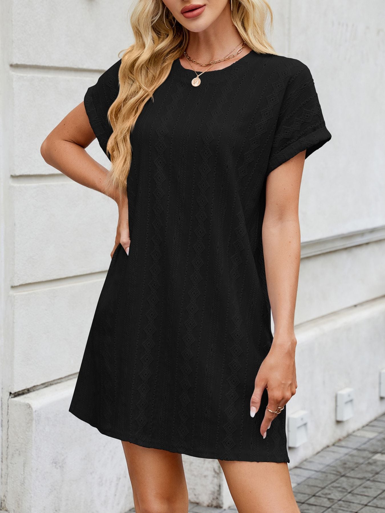 Woman wearing a black dress standing against a light-colored wall.