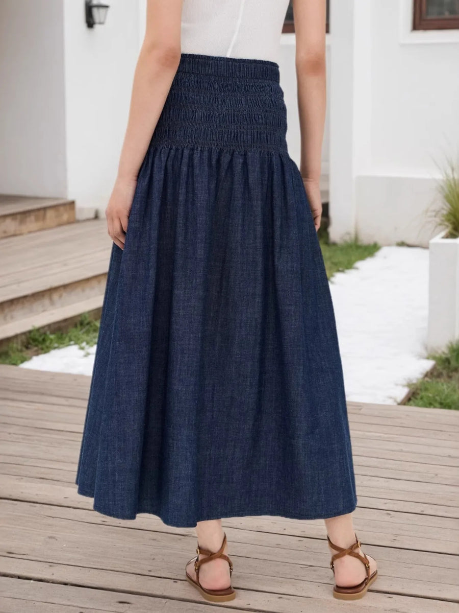 Person wearing a blue denim skirt standing on a wooden deck.