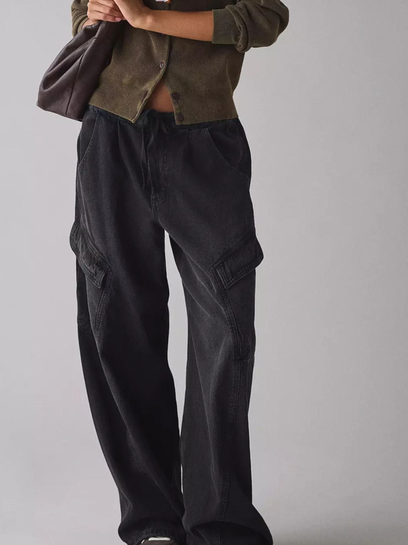 Person wearing dark cargo pants and a brown jacket on a plain background