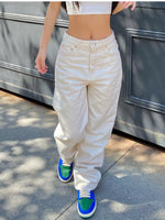 Person wearing white high-waisted pants and colorful sneakers on a sidewalk.