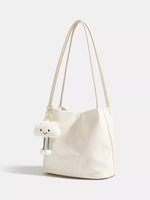 White handbag with a small white plush toy attached to it on a light gray background