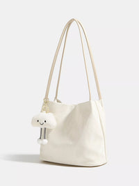 White handbag with a small white plush toy attached to it on a light gray background