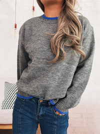 Person wearing a gray sweater with blue trim against a white wall.