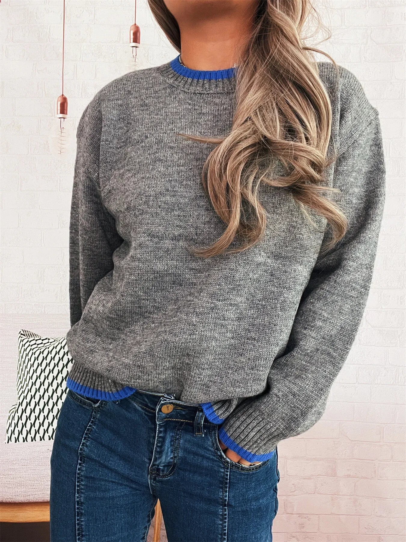 Person wearing a gray sweater with blue trim against a white wall.