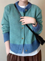 Person wearing a blue and green knitted cardigan holding a black bag.