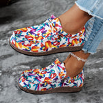 Colorful patterned shoes worn with denim jeans on a gray surface