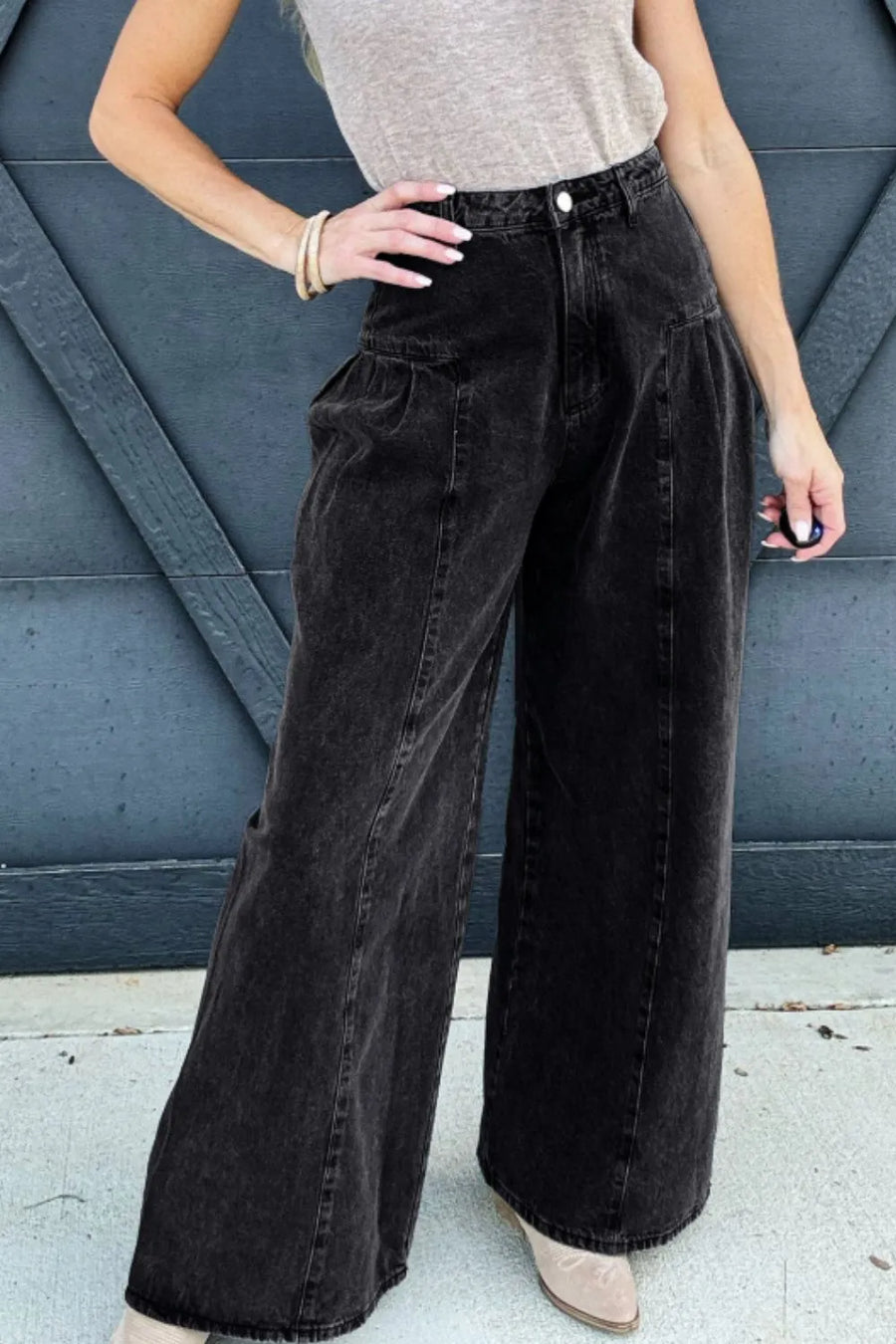 Person wearing black wide-leg pants and a beige top against a blue wall.