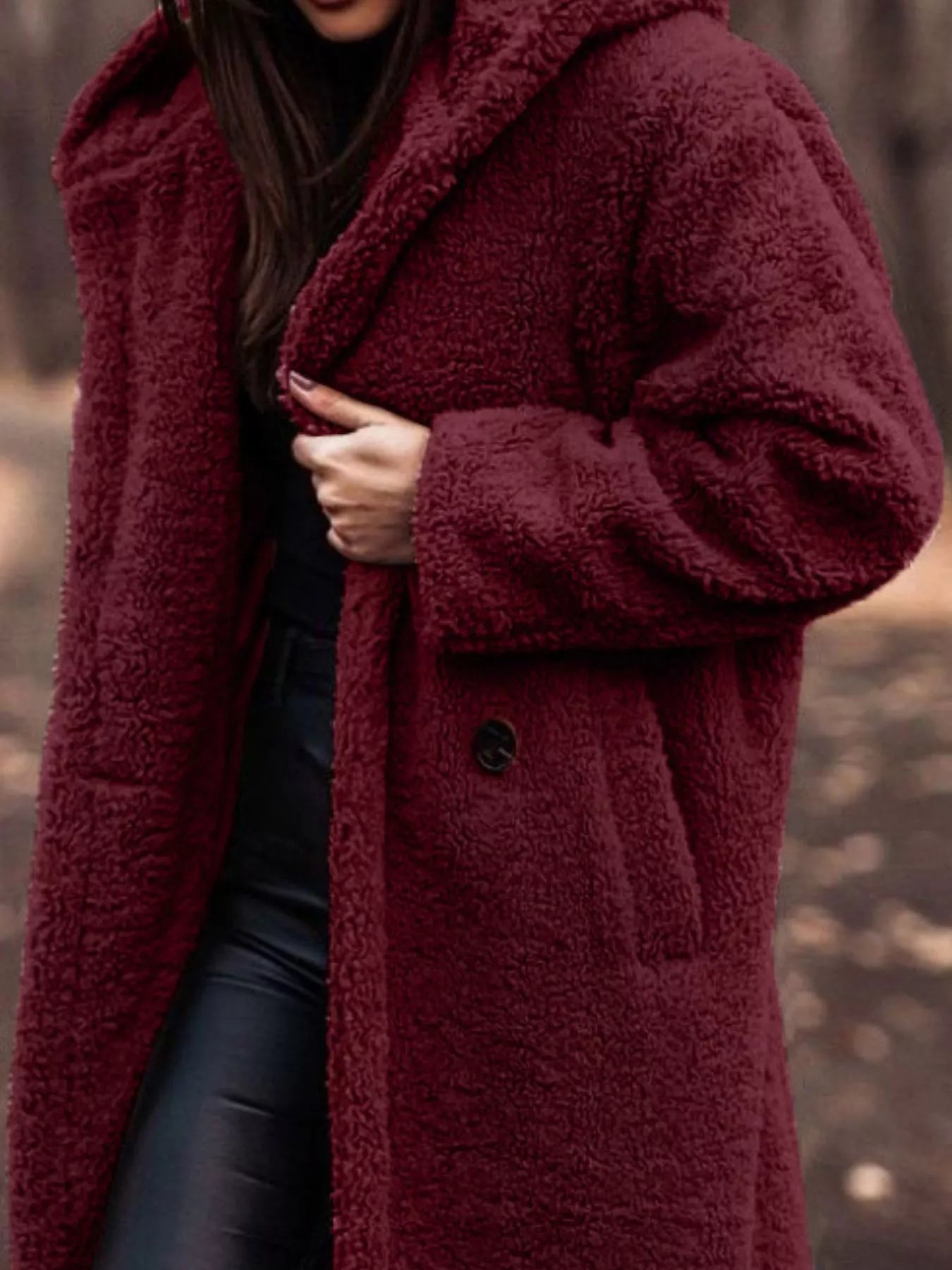 Person wearing a burgundy teddy coat with a blurred natural background