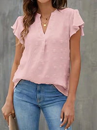 Person wearing a pink blouse with ruffled sleeves and blue jeans against a gray background