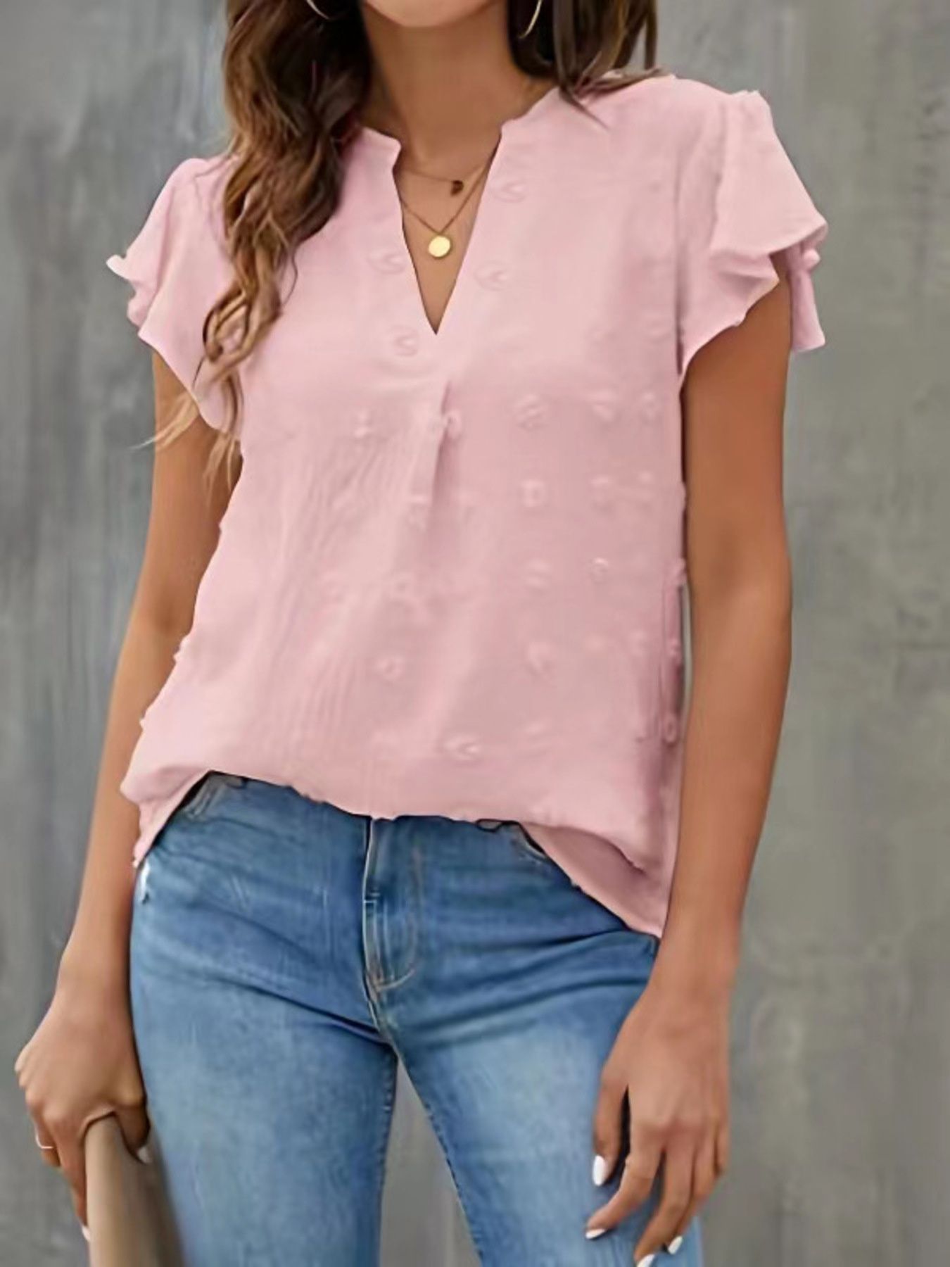 Person wearing a pink blouse with ruffled sleeves and blue jeans against a gray background