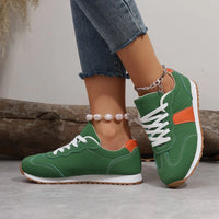 Green sneakers with orange accents worn by a person on a neutral background