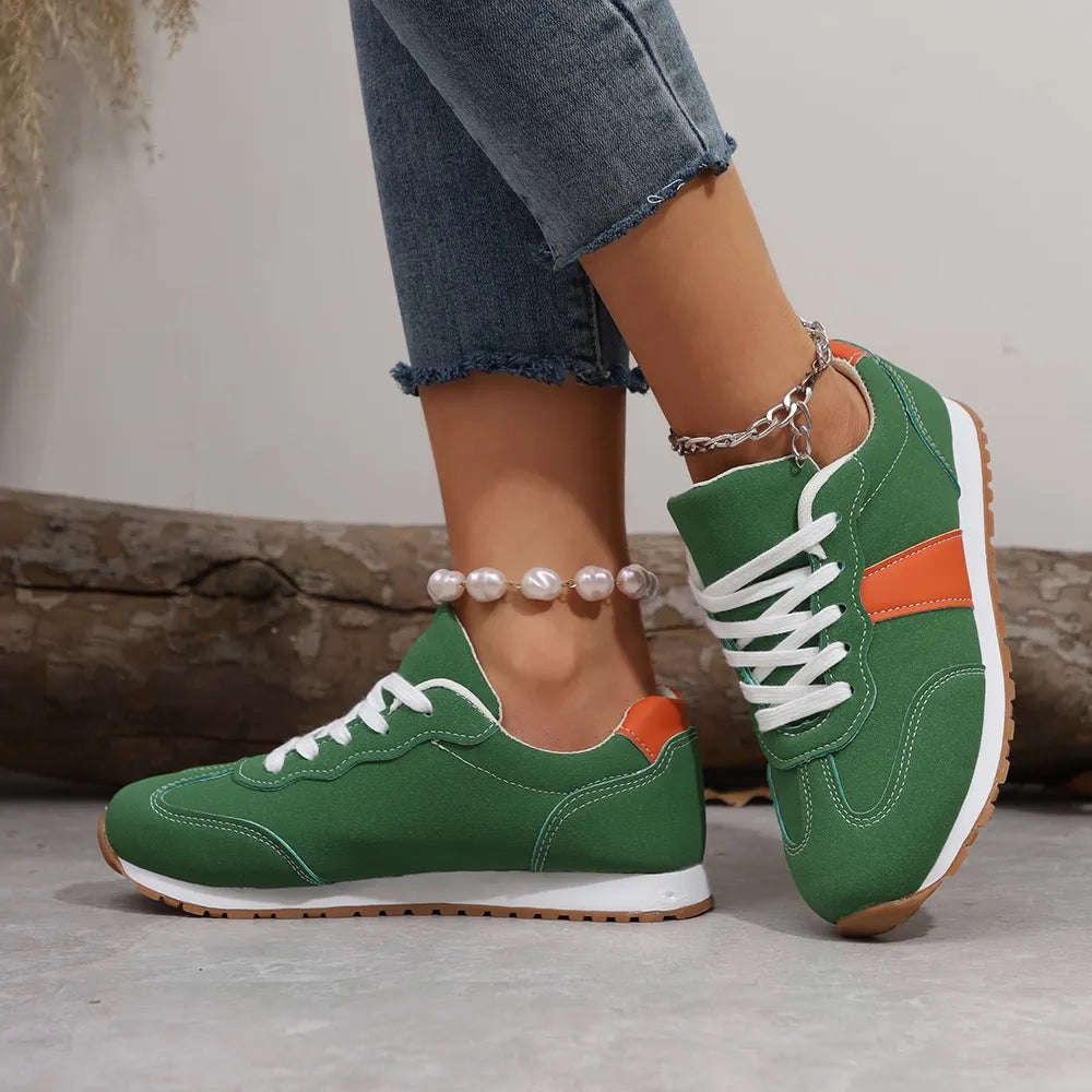 Green sneakers with orange accents worn by a person on a neutral background