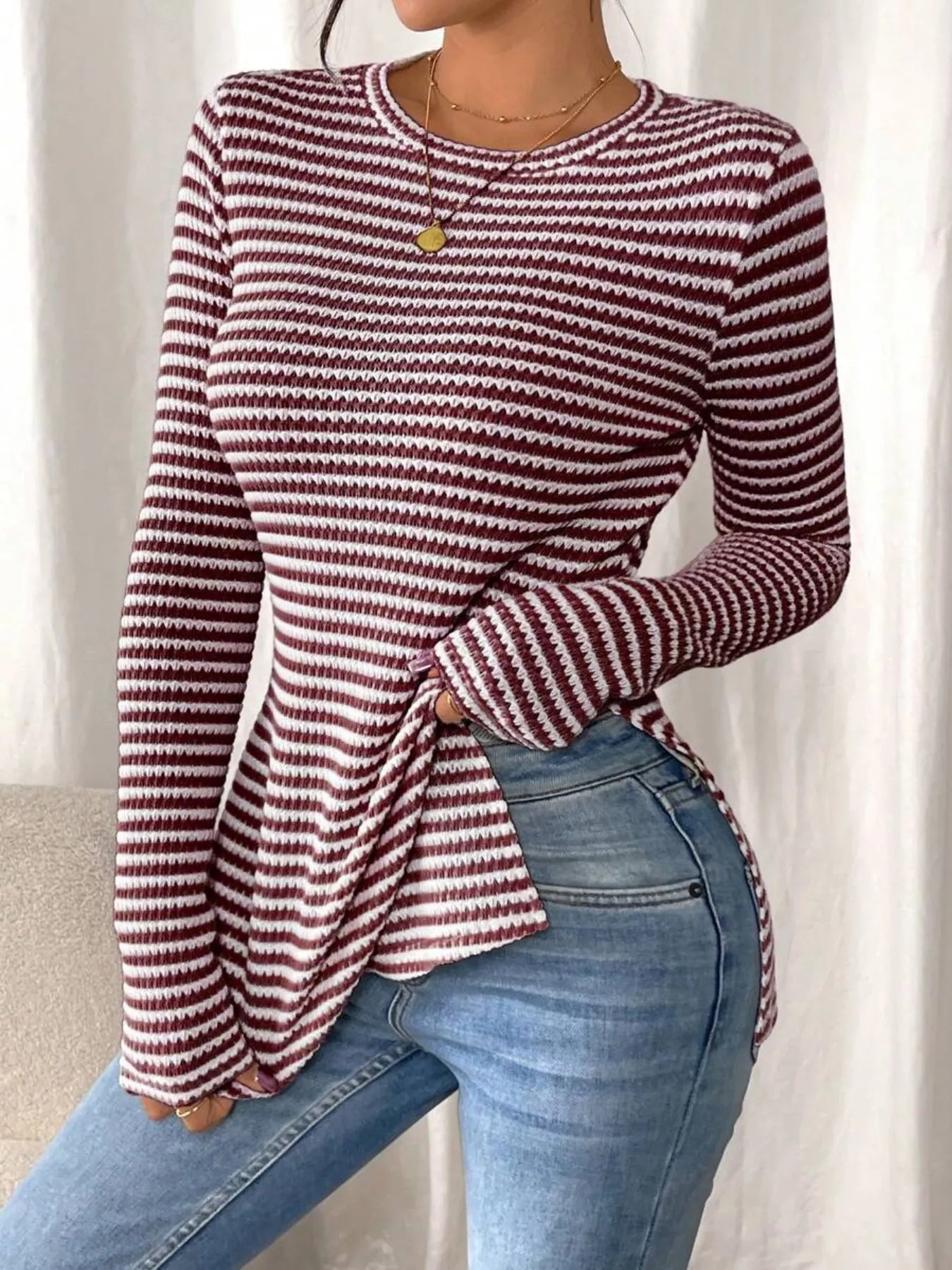 Person wearing a maroon and white striped sweater with blue jeans against a neutral background