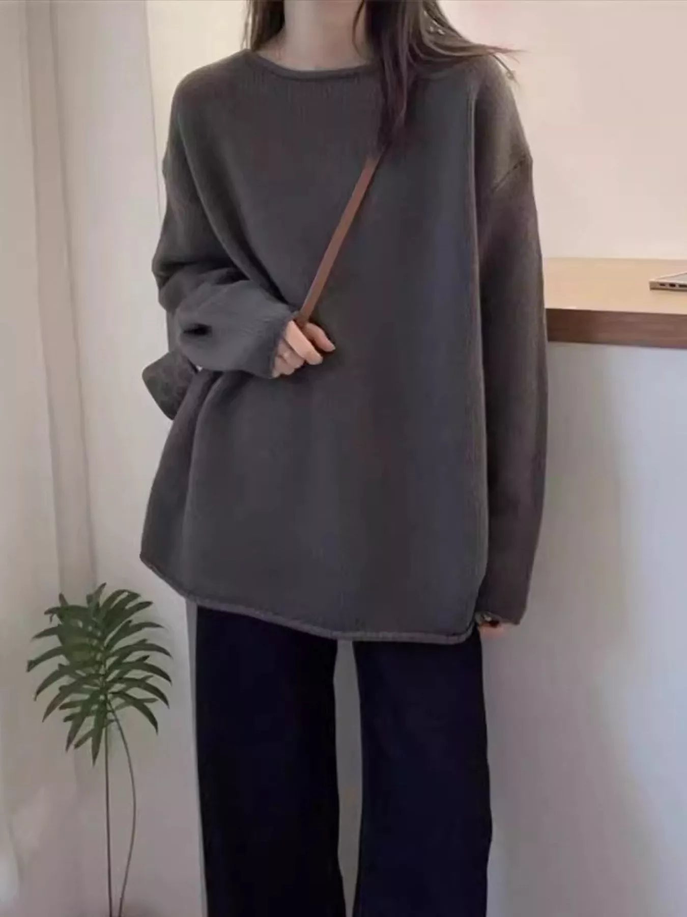 Person wearing a dark gray oversized sweater and black pants in a minimal indoor setting.