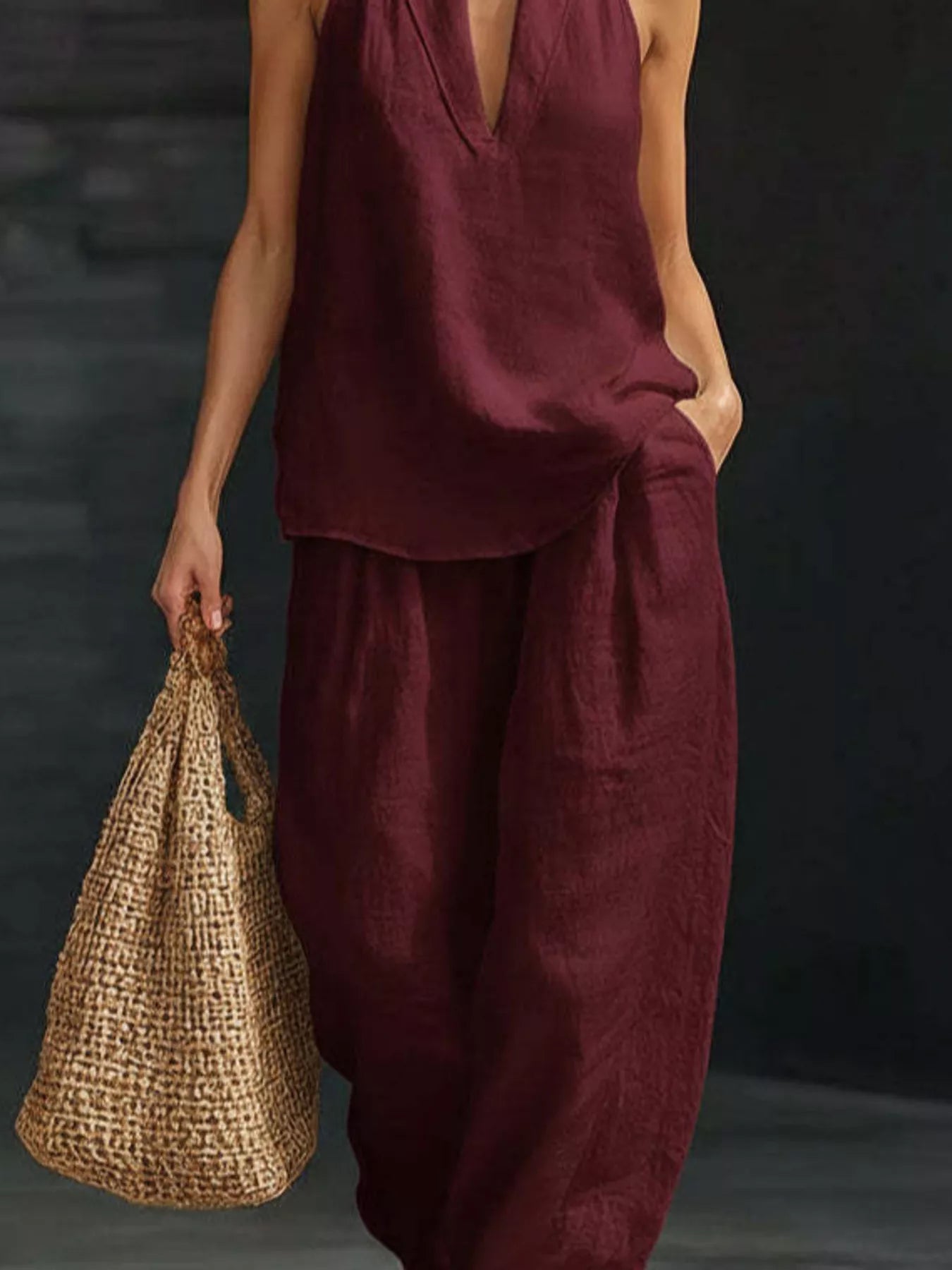 Person wearing a burgundy outfit holding a woven bag against a dark background