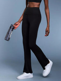 Person wearing black leggings and white sneakers holding a black water bottle with a brand logo on a gray background