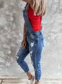 Person wearing blue distressed overalls and a red top against a gray concrete wall.