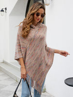 Woman wearing a colorful poncho and sunglasses, standing against a white wall.