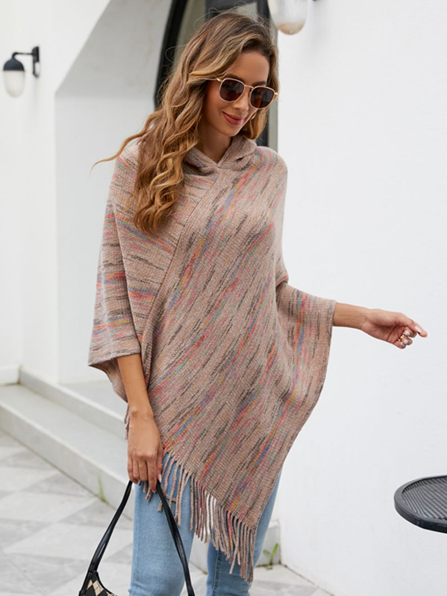 Woman wearing a colorful poncho and sunglasses, standing against a white wall.