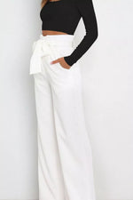 Person wearing a black long-sleeve top and white wide-leg pants on a plain background