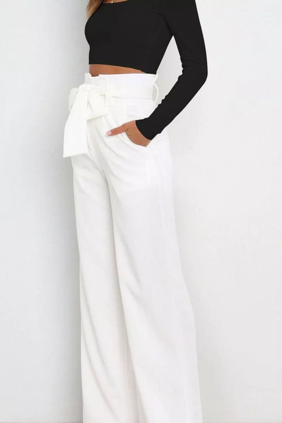 Person wearing a black long-sleeve top and white wide-leg pants on a plain background