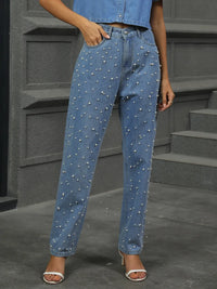 Person wearing blue jeans with pearl embellishments on a gray background