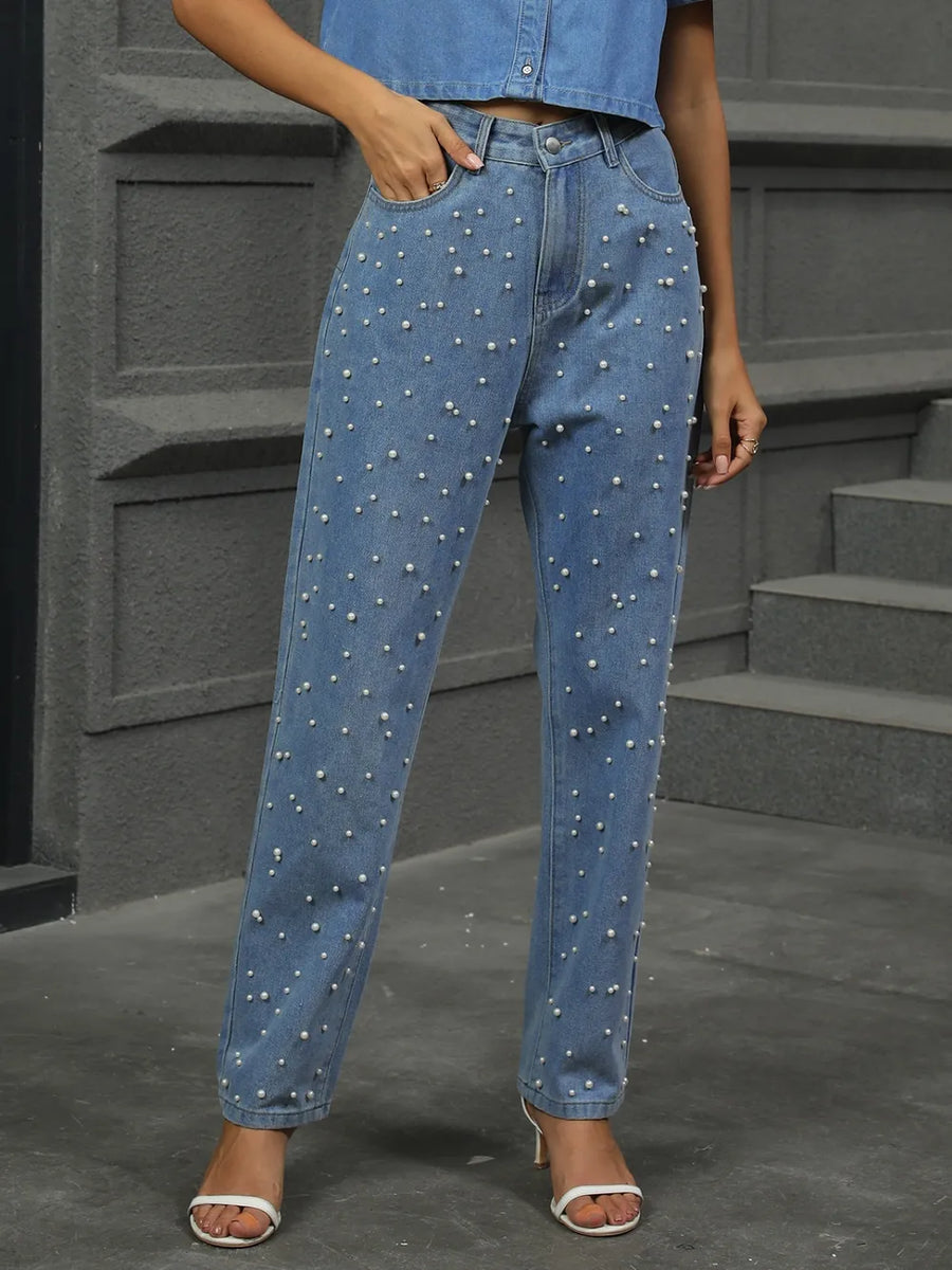 Person wearing blue jeans with pearl embellishments on a gray background