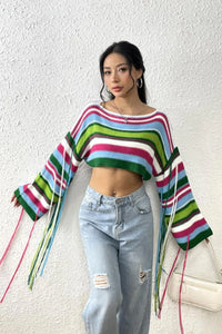 Person wearing a colorful striped sweater and jeans against a white wall.
