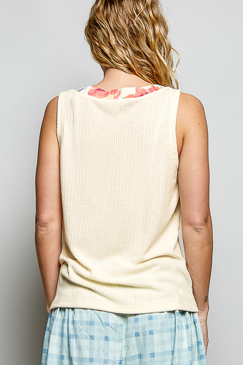 Person wearing a beige sleeveless top with floral pattern on the back, standing against a plain background.