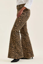 Leopard print flared pants worn with a white shirt on a beige background