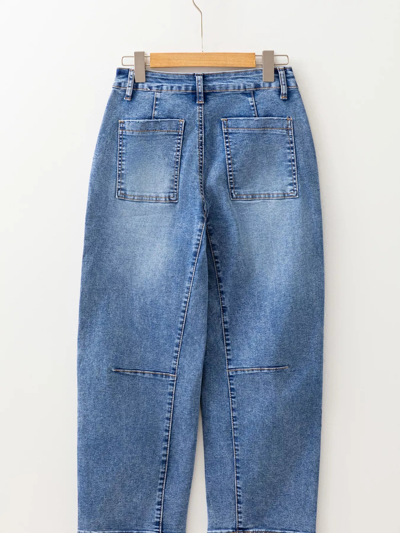 Blue jeans hanging on a wooden hanger against a white background