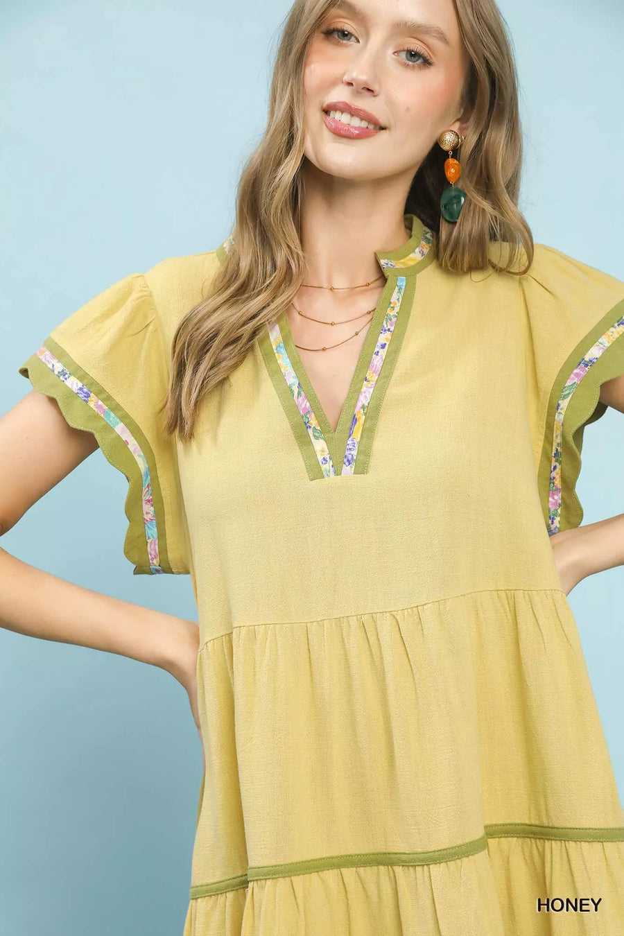 Woman wearing a yellow dress with floral embroidery on a light blue background