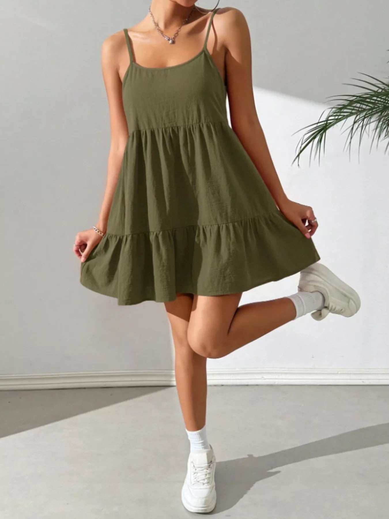 Woman wearing an olive green dress with white sneakers against a plain background