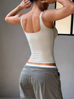 Person wearing a white tank top and gray pants against a neutral background