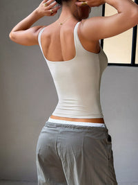 Person wearing a white tank top and gray pants against a neutral background