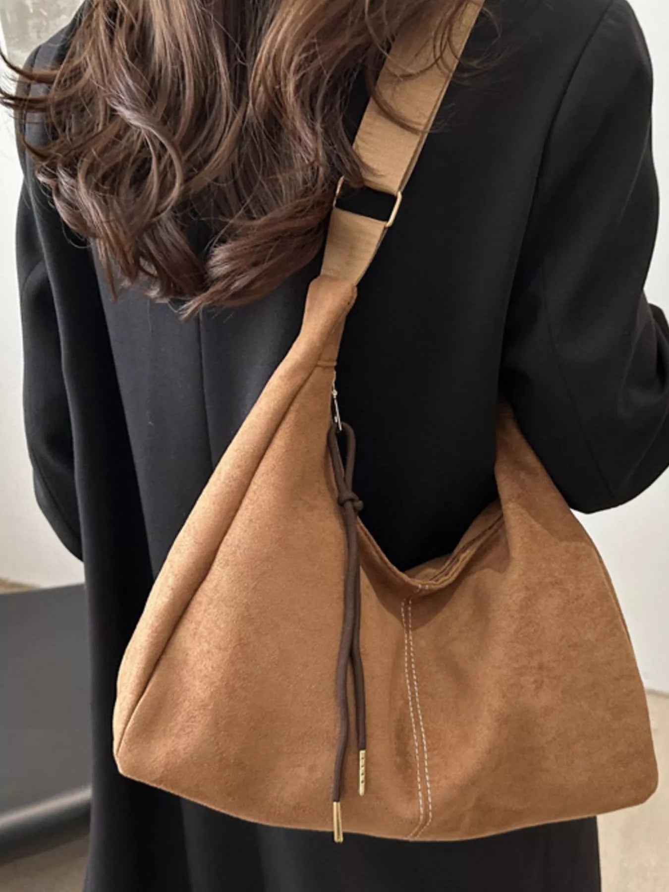 Brown leather shoulder bag worn by a person with a neutral background