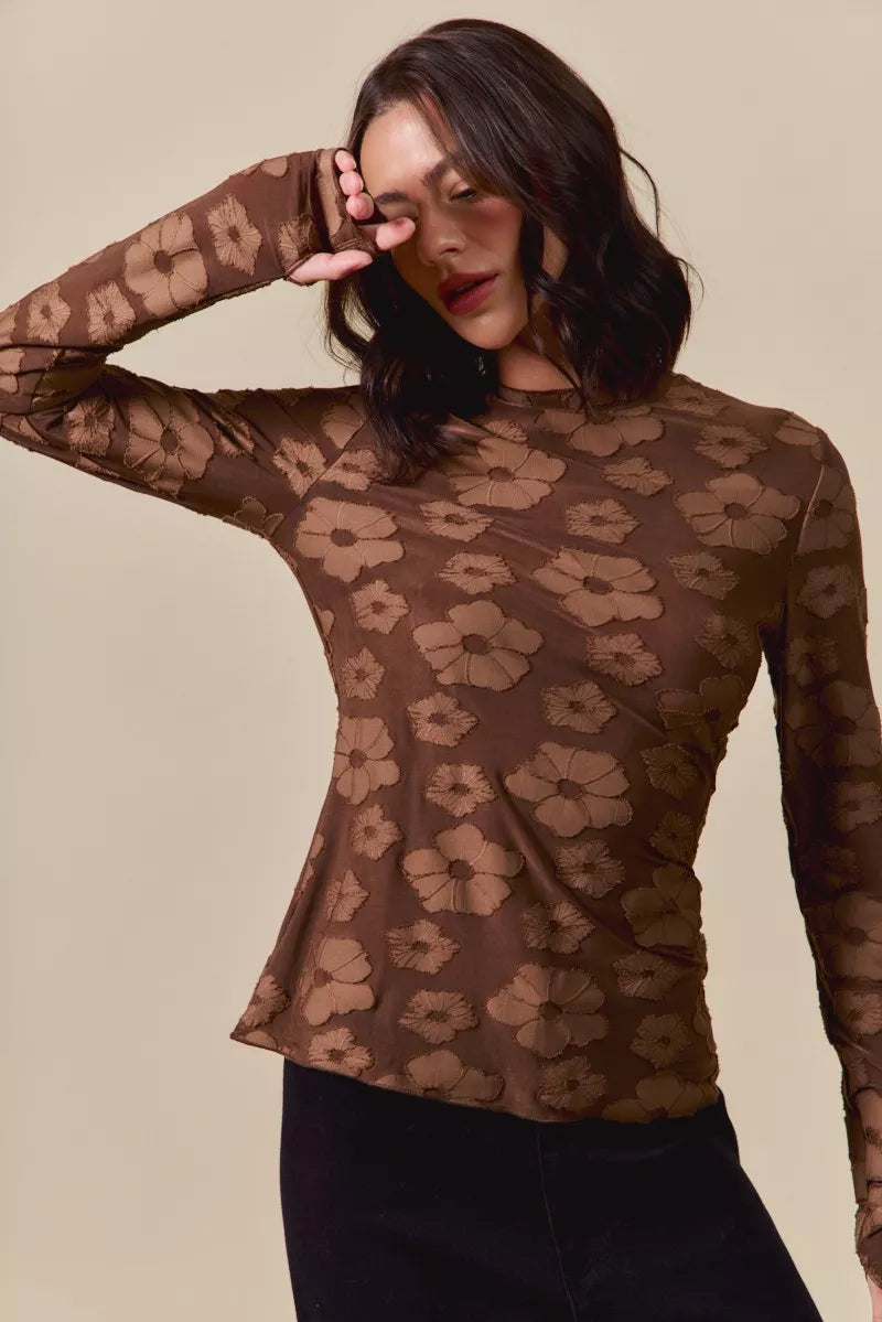 Woman wearing a sheer brown floral patterned top against a beige background