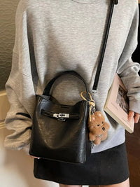 Person holding a black backpack with a teddy bear keychain and a book, wearing a gray sweatshirt and black skirt.