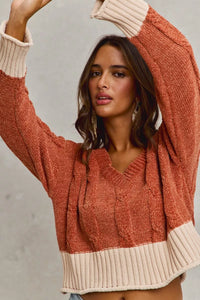 Woman wearing a rust-colored cable knit sweater with beige cuffs and hem against a neutral background