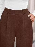 Brown pleated pants worn with a white top on a neutral background