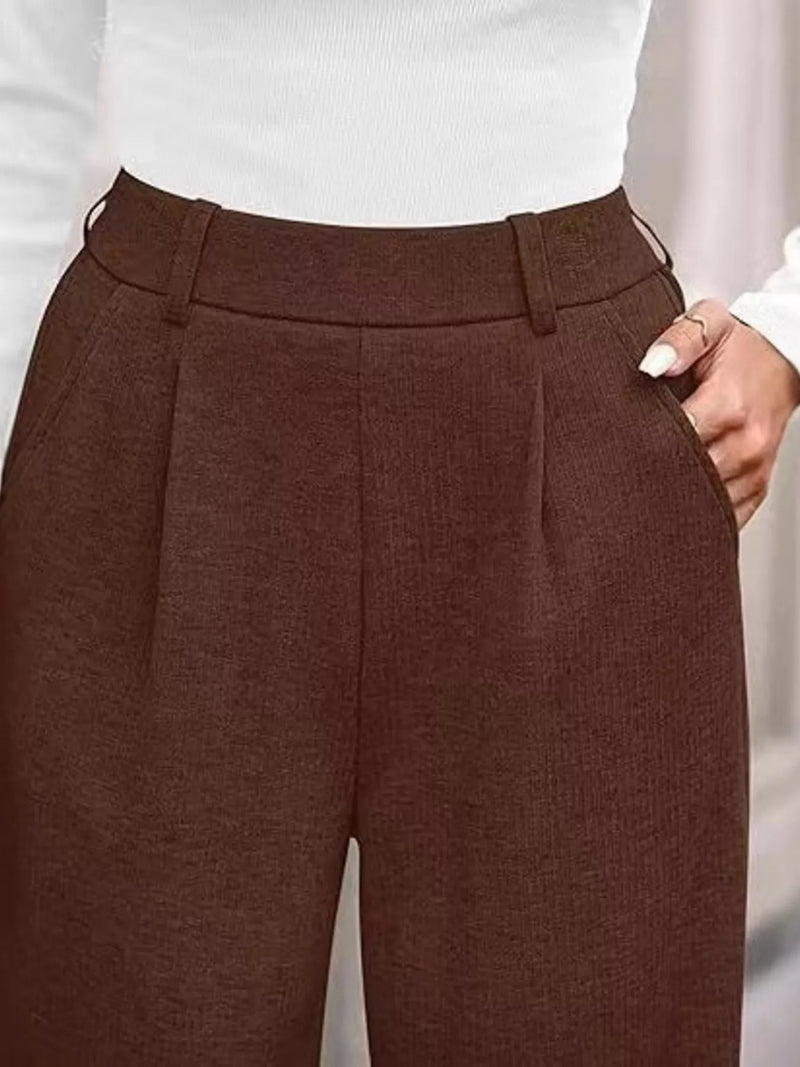 Brown pleated pants worn with a white top on a neutral background