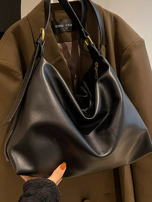 Black leather handbag held by a person wearing a brown coat with 'Chic Van' branding.