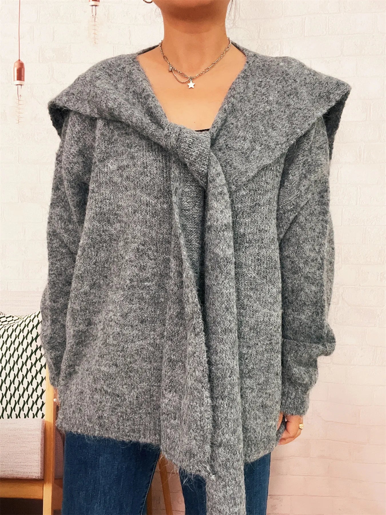 Person wearing a gray hooded cardigan with a neutral background