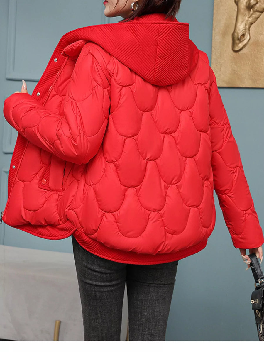 A person wearing a bright red quilted puffer jacket with a hood, shown from the back in an indoor setting with a blue wall and framed art in the background.