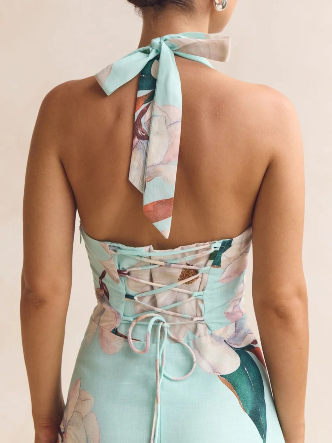 Woman wearing a floral dress with a neck scarf on a plain background