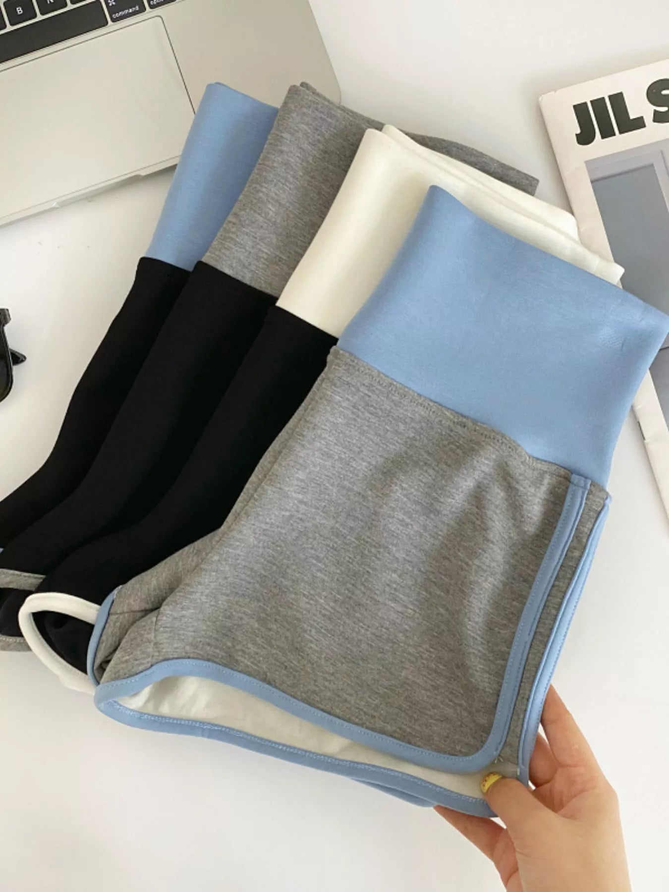 Set of folded towels in black, gray, and blue held by a hand on a white surface.