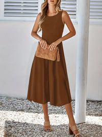 Woman wearing a brown dress holding a matching handbag against a white background